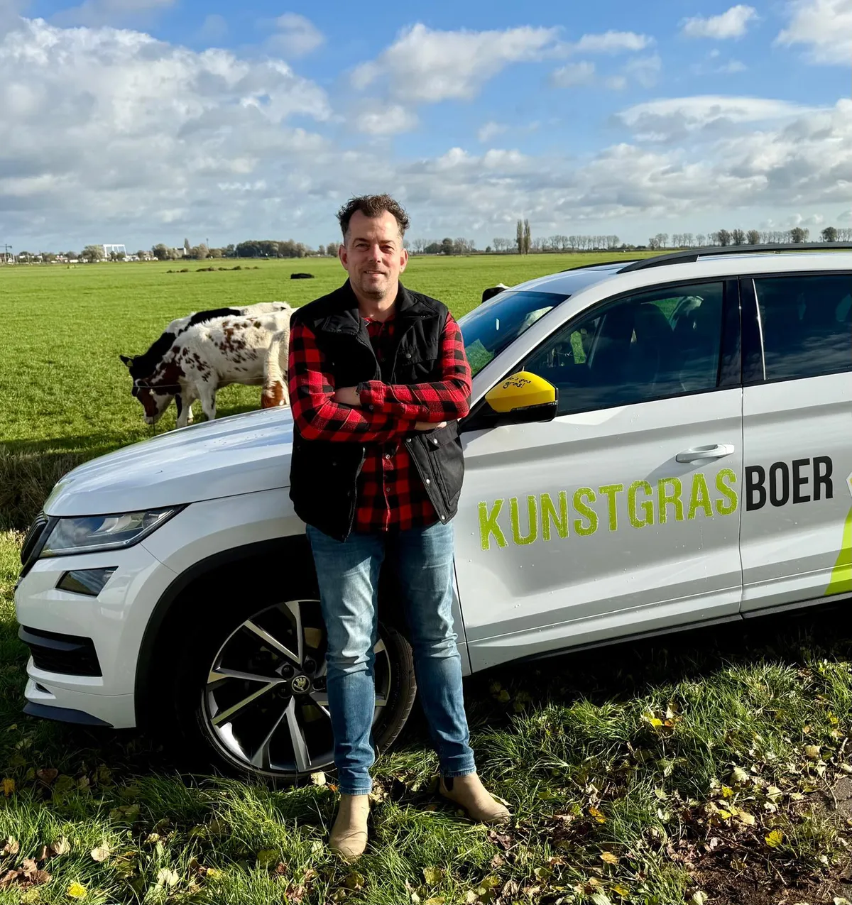 Boer Henrik van Kunstgrasboer bij de bedrijfsauto, met koeien in het weiland op de achtergrond