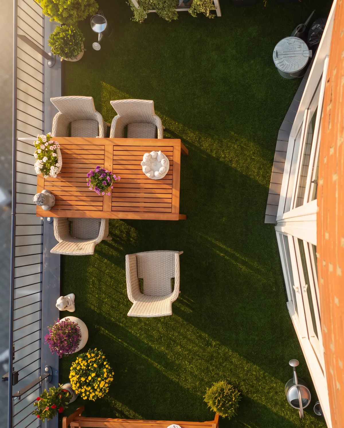 Bovenaanzicht van een compacte tuin met kunstgras, een houten eettafel met stoelen en bloembakken langs de schutting