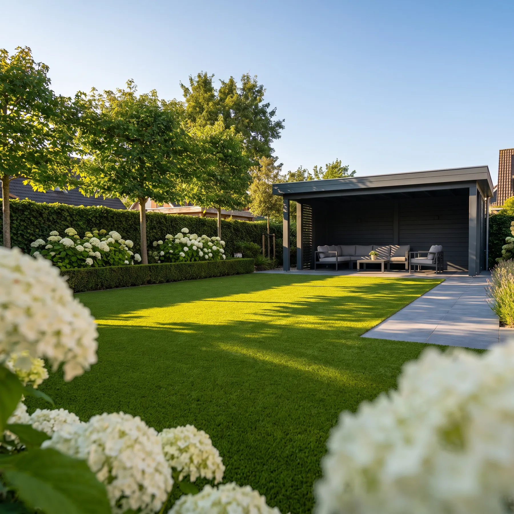 Ruime achtertuin met een strak kunstgrasgazon, een moderne overkapping met loungeset en bloeiende hortensia's